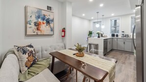 Una sala moderna con un sofá gris, una mesa de comedor de madera y una cocina al fondo.