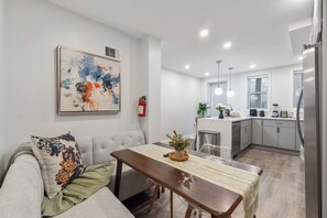 Ein modernes Wohnzimmer mit einem grauen Sofa, einem Holzessttisch und einer Küche im Hintergrund.