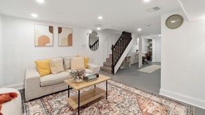 Una sala moderna con sofá, mesa de centro y alfombra estampada. Una escalera conduce a otra habitación.