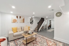 Ein modernes Wohnzimmer mit einer Couch, einem Couchtisch und einem Teppich mit Muster. Eine Treppe führt in einen anderen Raum.