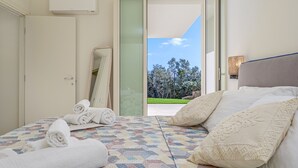 A bedroom with a bed, towels, a mirror, and a view of trees through an open door.
