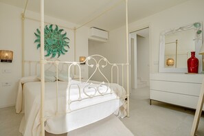 Een hemelbed met een witte baldakijn, een witte ladenkast met spiegel, en een decoratief wandobject.