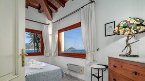 Ein Schlafzimmer mit Bett, einem Fenster mit Vorhängen, einem Heizkörper, einem Holzschrank und einem Tisch.