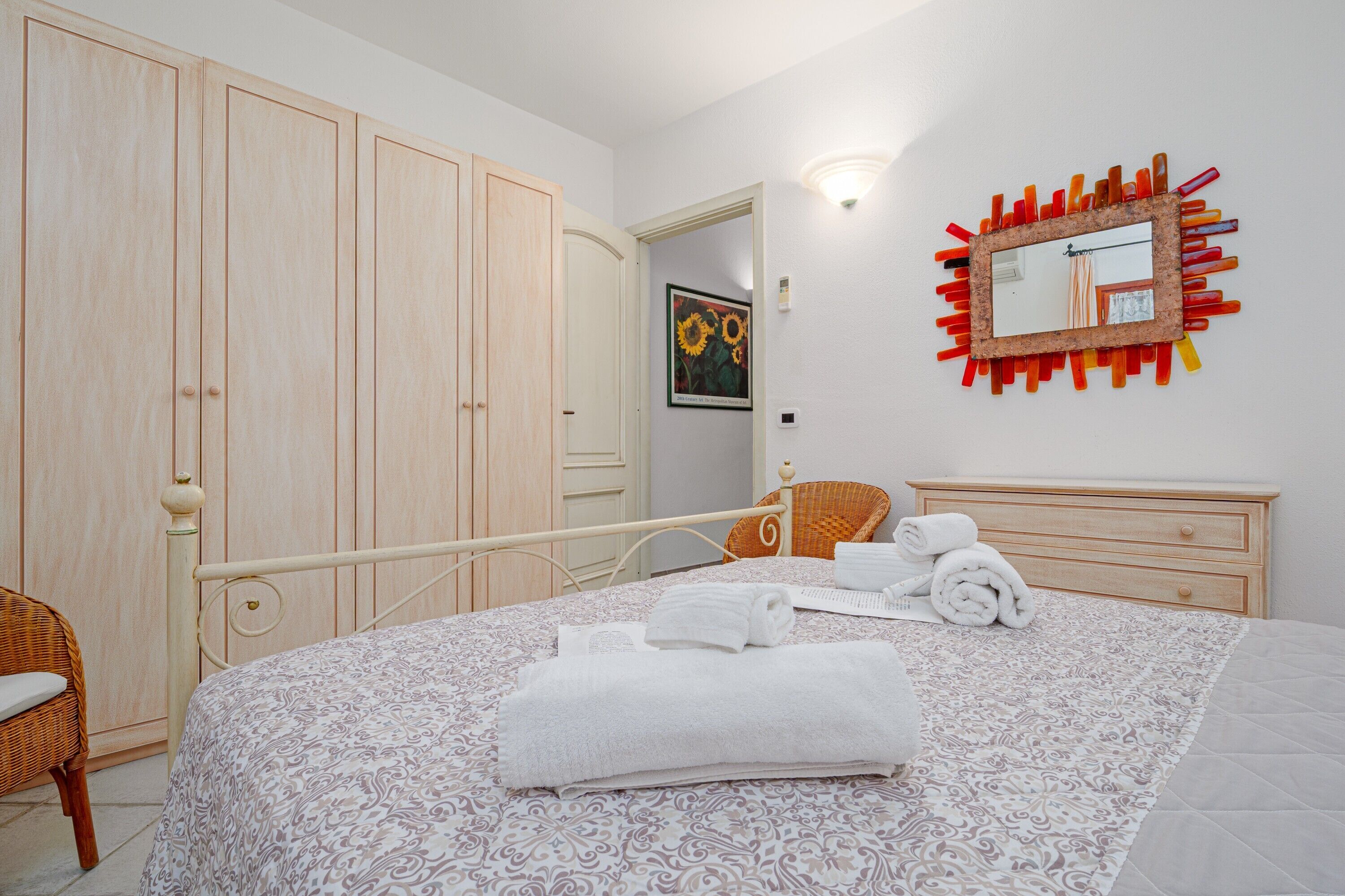 Une chambre à coucher comprenant un lit, une armoire en bois, un miroir et un luminaire fixé au mur.
