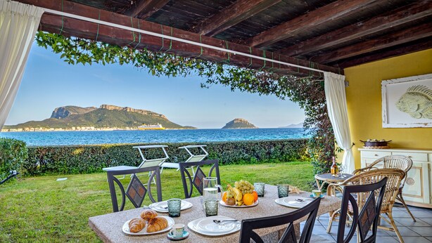 Ein Essbereich im Freien mit Blick auf das Meer und die Hügel, komplett mit einem Tisch, der mit Croissants, Obst und einer Kanne bestückt ist.