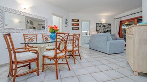 Ein Essbereich mit Korbstühlen, einem Glastisch, einem grauen Sofa und einem Holzschrank.