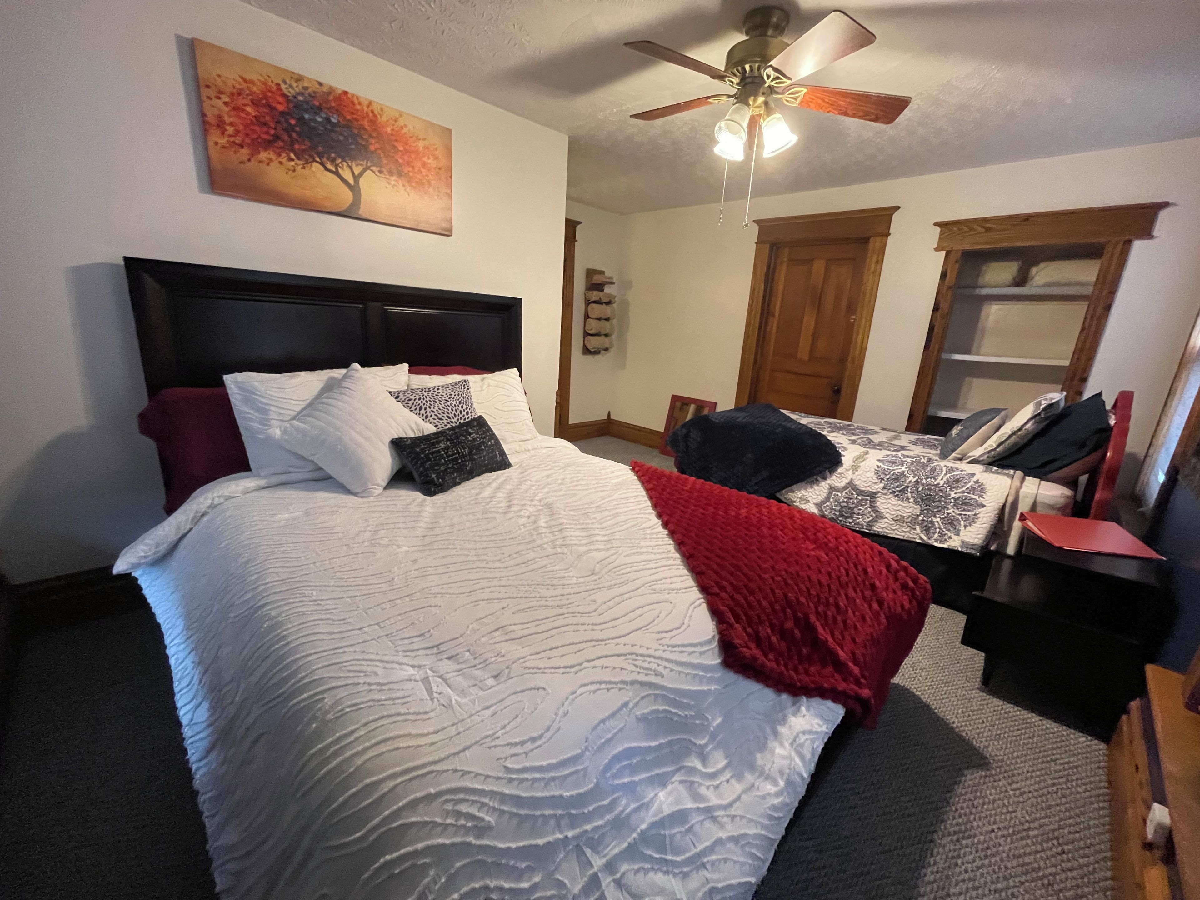 A bedroom with a bed, a ceiling fan, a painting, and a window.