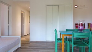 Ein Zimmer mit einem Bett, einem Esstisch mit Stühlen, einer Glasvase und einem Kleiderschrank.