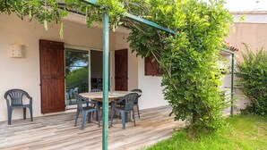 Eine Terrasss mit Holztable und -stühlen, einer Pergola und einem grünen Busch.