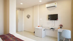 A hotel room with a bed, a desk, a chair, an air conditioner, a television, and a small cabinet. - Hotel Joystel Studio (Jaipur)