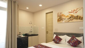 A bedroom with a bed, pillows, a painting, a door, and a bathroom with a sink and mirror. - Hotel Joystel Studio (Jaipur)