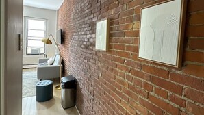 Ein Flur mit freiliegenden Backsteinwänden, einem gerahmten Kunstwerk, einem Mülleimer und einem modernen Sessel.
