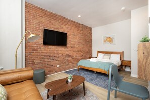 A modern bedroom with a brick wall, a bed, a sofa, a desk, and a television. - Peaceful Back Bay Studio (Boston)