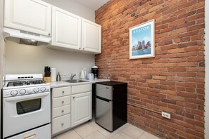 A compact kitchen with a gas stove, oven, white cabinets, a black refrigerator, and a brick wall. - Peaceful Back Bay Studio (Boston)