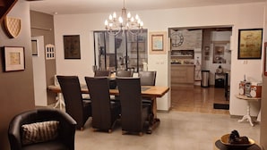 Ein Essbereich mit einer Chandelier, einem Holztisch und Stühlen. Eine Küche ist durch eine offene Tür sichtbar.