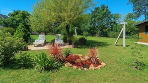 Ein gepflegter Garten mit zwei Liegestühlen, einem kleinen Baum und einer Steinskulptur.