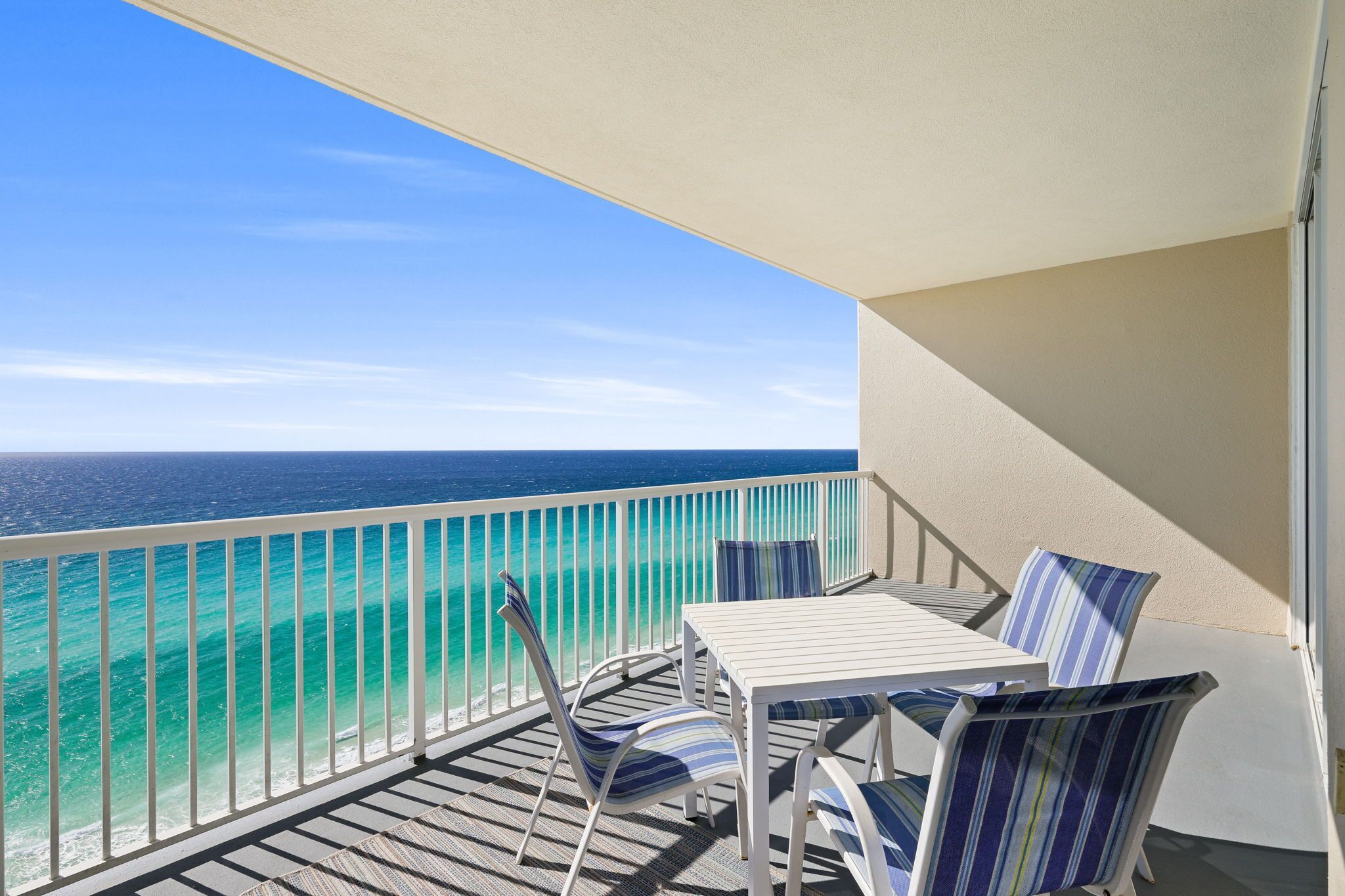 Un balcon avec une table blanche et des chaises à rayures, donnant sur une mer turquoise.