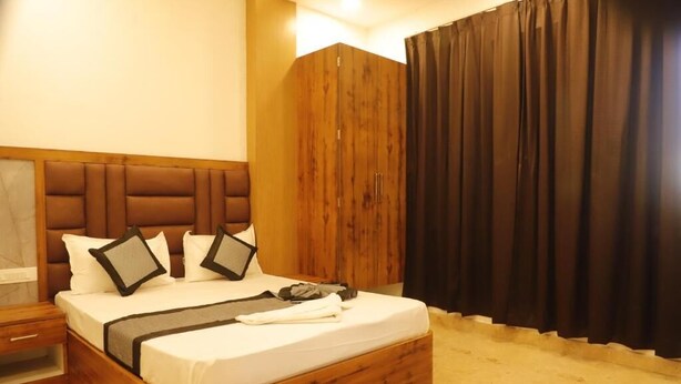 A neatly made bed with a wooden headboard, a bedside table, and a large window with curtains. - THE BLESSING PALACE (Muzaffarpur)