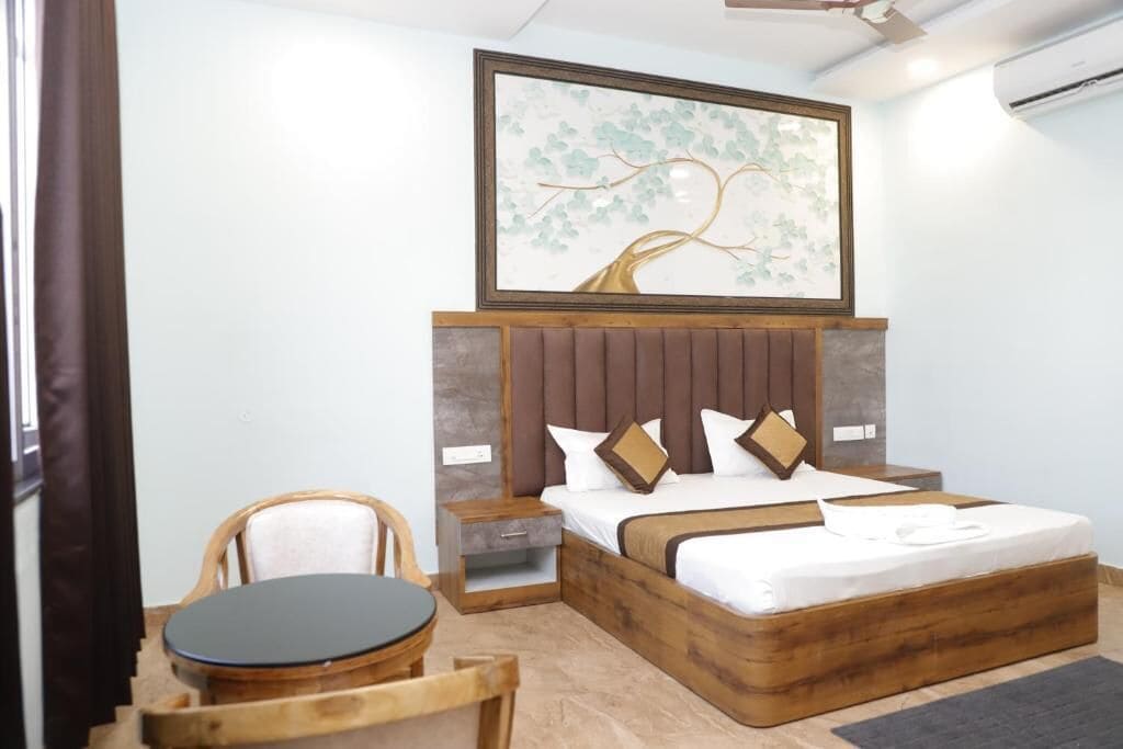 Un dormitorio con cabecera de madera, cama con ropa blanca, mesita de noche, silla de madera y una mesa redonda.