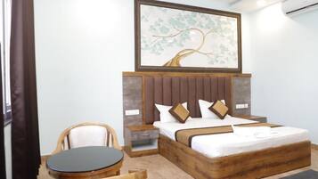 Un dormitorio con cabecera de madera, cama con ropa blanca, mesita de noche, silla de madera y una mesa redonda.