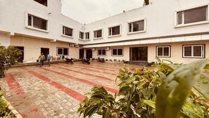 A courtyard with a tiled floor, potted plants, and a building with multiple windows and a door. - THE BLESSING PALACE (Muzaffarpur)