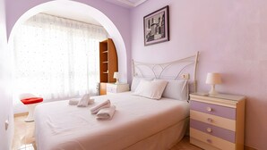 Une chambre à coucher bien rangée, avec un lit, des tables de chevet, une commode, une chaise et une fenêtre avec des rideaux.