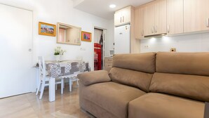 Un salon avec un canapé beige, une table à manger avec des chaises et un coin cuisine doté de meubles en bois.