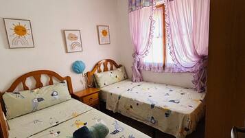 A bedroom with two beds, a chandelier, and a window with curtains.
