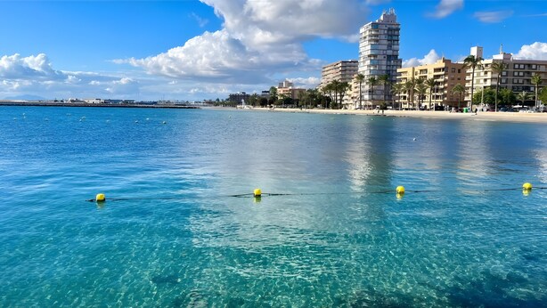 Un paysage urbain côtier avec une eau bleue et limpide, une plage de sable et des bâtiments modernes.