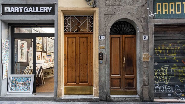 A building with a wooden door marked with the number 10, adjacent to a shop named "Art Gallery" and another shop with graffiti on the shutter. - Casa Musa by MMega (Florence)