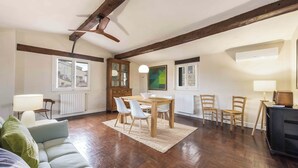 A spacious living room with a wooden dining table, white chairs, a sofa, and a ceiling fan. - Casa Musa by MMega (Florence)