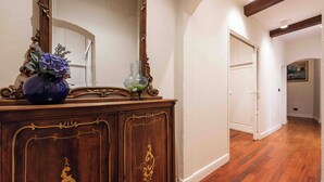 A hallway with wooden flooring, a wooden cabinet with ornate carvings, and a large mirror. - Casa Musa by MMega (Florence)