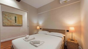 A neatly made bed with towels, a wall art piece, a standing lamp, and a wicker basket. - Casa Musa by MMega (Florence)
