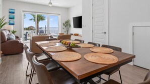 Uma sala de jantar espaçosa com uma longa mesa de madeira, várias cadeiras e jogos americanos de palha.
