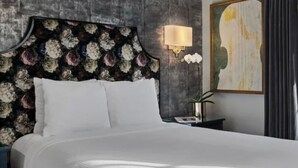 Een net opgemaakt bed met witte lakens, een donker bloemenpatroon hoofddeksel en een wandlamp.