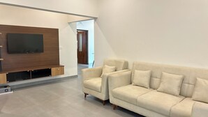 Una sala de estar moderna con un televisor de pantalla plana grande montado en una pared de madera, un sofá beige con varios cojines y un diseño minimalista.