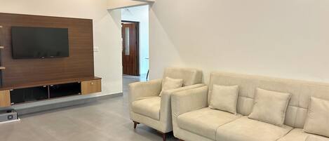 Una sala de estar moderna con un televisor de pantalla plana grande montado en una pared de madera, un sofá beige con varios cojines y un diseño minimalista.