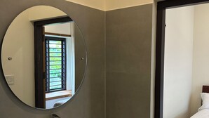 Un baño moderno con un espejo redondo, un lavabo blanco y vistas al dormitorio contiguo.
