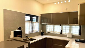 Una cocina moderna con armarios oscuros, horno empotrado, lavamanos y una ventana con cortinas.