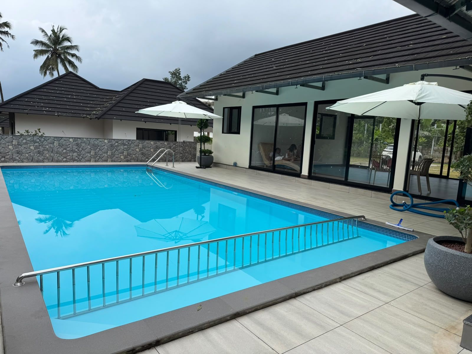 Ein Schwimmbecken mit Metallschutzgitter, umgeben von einer Steinmauer und einer gefliesten Terrasse.