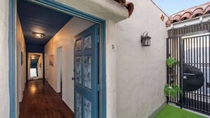 A hallway with a blue door, a black gate, and a small garden area. - Check in with a Cocktail | Heart of Hermosa Beach (Hermosa Beach)