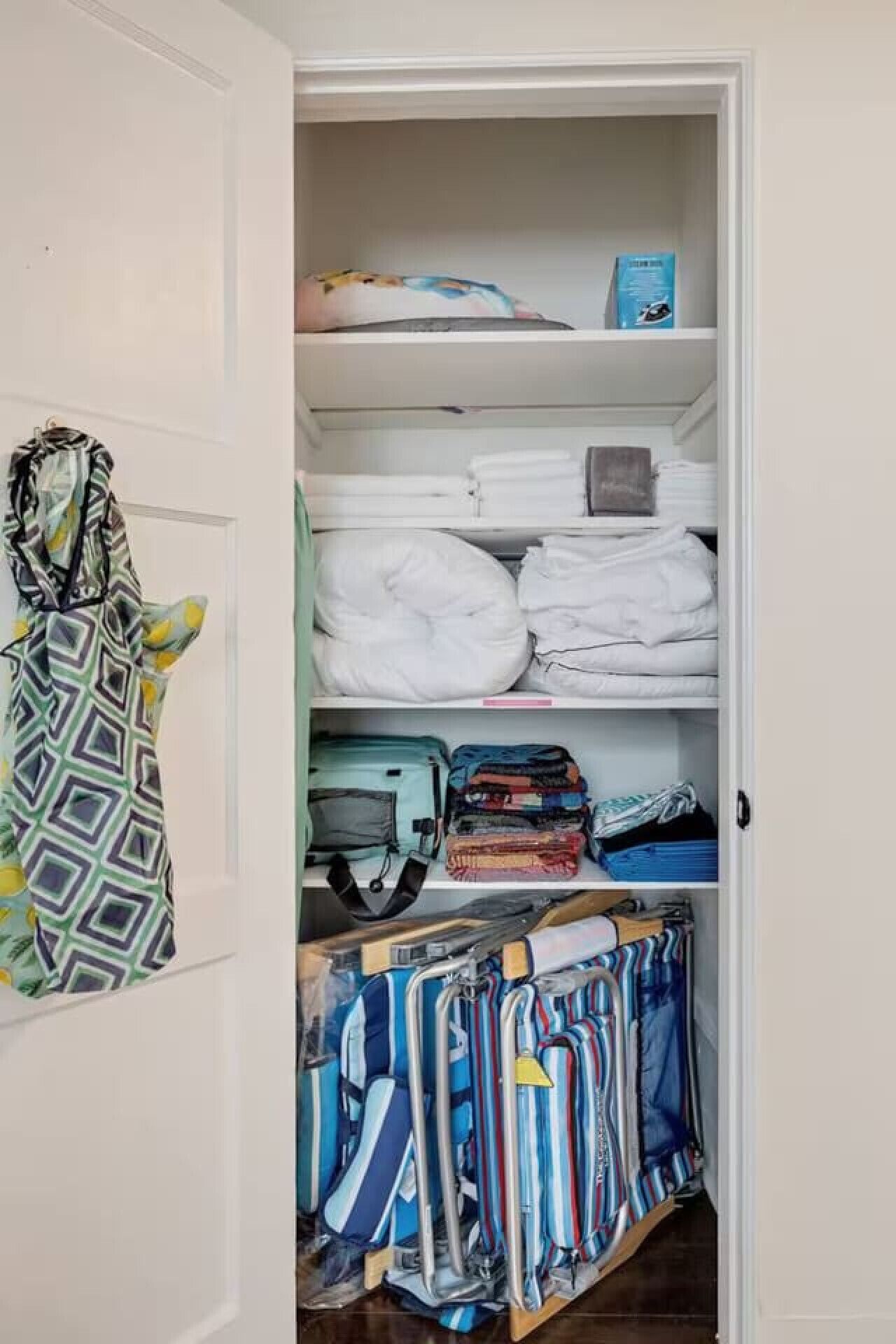 Um armário com roupas bem dobradas, uma peça pendurada e uma mala.