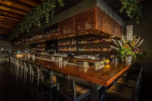 A bar with a wooden counter, metal shelves with bottles, and chairs. - Check in with a Cocktail | Heart of Hermosa Beach (Hermosa Beach)