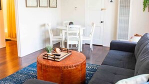 A living room with a round coffee table, a gray sofa, and a dining area with white chairs and a table. - Check in with a Cocktail | Heart of Hermosa Beach (Hermosa Beach)