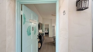 Un corridoio con una porta blu chiaro contrassegnata dalla lettera 'B' e un cartello con su scritto 'Vietato l'accesso', che conduce a una stanza con un letto e una finestra.