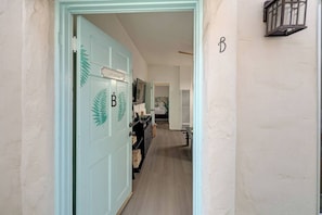 Ein Korridor mit einer hellblauen Tür, die mit einem 'B' gekennzeichnet ist und ein Schild mit der Aufschrift 'Betreten Verboten' trägt, der zu einem Raum mit einem Bett und einem Fenster führt.