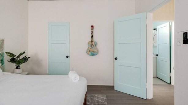 Una camera da letto con un letto, una chitarra, due porte color azzurro chiaro e una pianta.