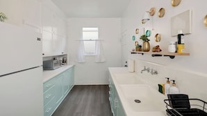 Una cucina moderna con mobili bianchi, un lavello doppio e una finestra con tende bianche.