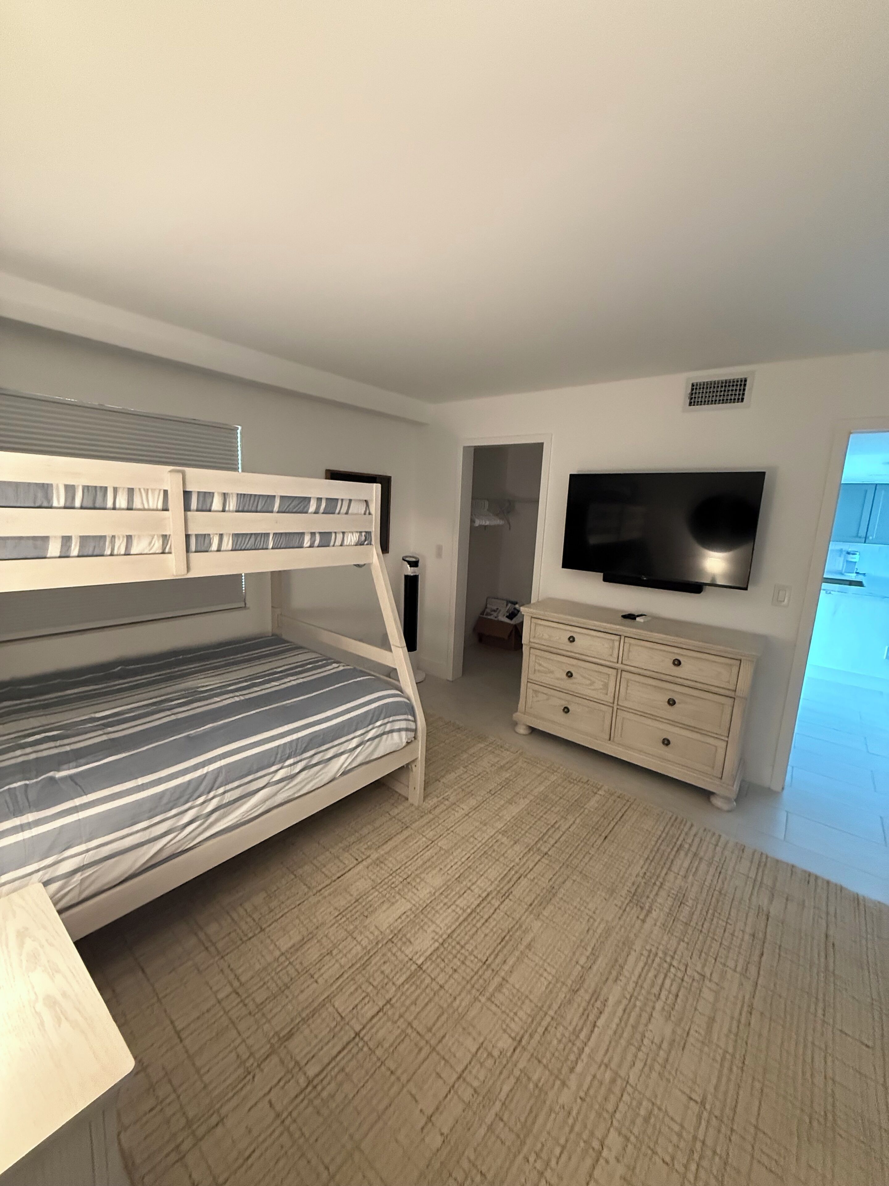 A bedroom with a bunk bed, a TV mounted on the wall, and a dresser.
