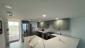A modern kitchen with a marble countertop, stainless steel appliances, and a view to the outside. - Charming beachfront condo, Daytona Beach Shores (Daytona Beach Shores)
